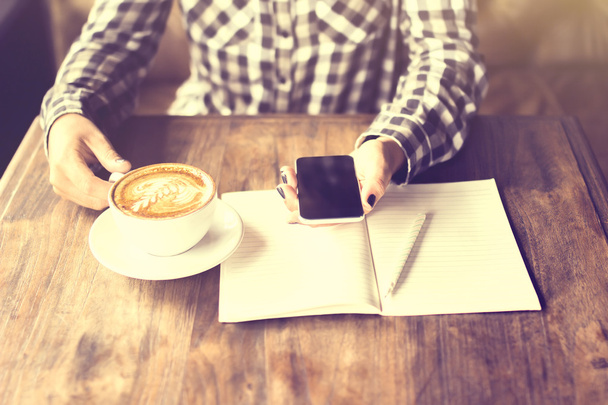 Mãos de menina com telefone celular, cappuccino e diário em branco com penc
 - Foto, Imagem