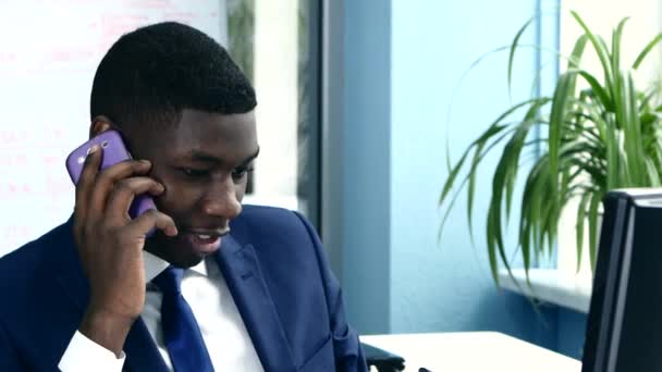 African American biznesmen na telefon siedzi przy komputerze - Materiał filmowy, wideo