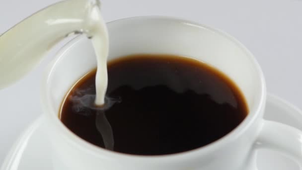 Pouring milk into cup with coffee on a white background, slow motion, close up - Filmati, video