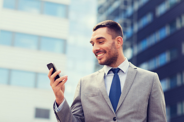 smiling businessman with smartphone outdoors - Foto, afbeelding