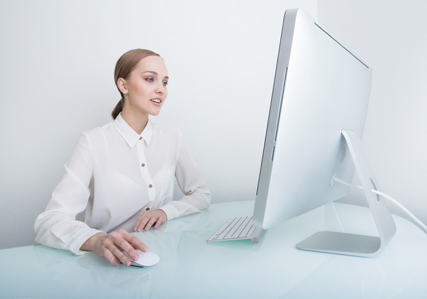 Attractive smiling young business woman working on computer in the office at the desk - Фото, зображення