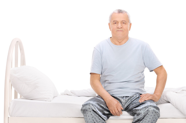 Senior man in pajamas sitting on a bed - Foto, imagen