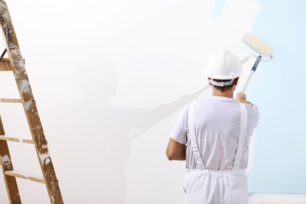 Ζωγράφος άνθρωπο στο χώρο εργασίας με ένα κυλινδρικό χρωστήρα στον τοίχο - Φωτογραφία, εικόνα