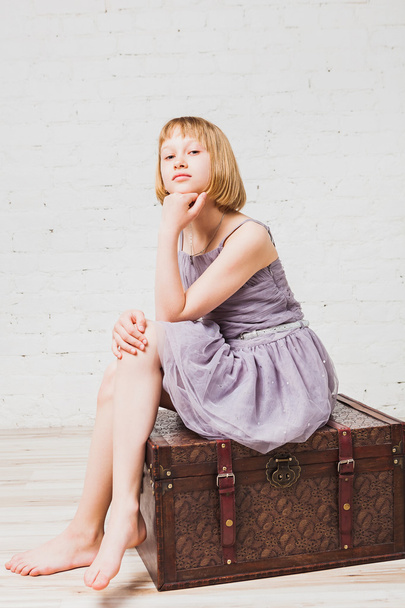Well-dressed girl sitting on old box - Foto, imagen