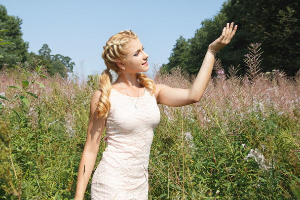 Pretty young blonde girl on blossoming field in a summer - Foto, Bild
