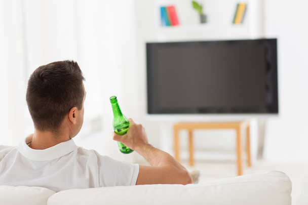man watching tv and drinking beer at home - 写真・画像