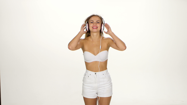 Όμορφο θηλυκό στα ακουστικά ακούγοντας τη μουσική με το φτερουγίσματα στα μαλλιά του ανέμου πάνω από το λευκό φόντο - Πλάνα, βίντεο