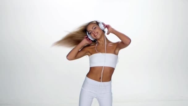 Beautiful female in headphones listening to the music with fluttering on the wind hair over white background. Slow motion. - Materiał filmowy, wideo