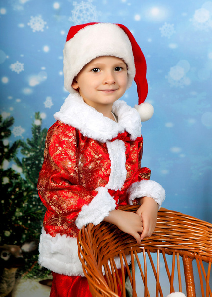 красивий маленький хлопчик в червоному костюмі і кепці в різдвяному декорі
 - Фото, зображення