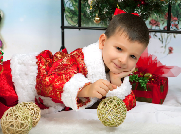 красивый маленький мальчик в красном костюме в новогодних украшениях
 - Фото, изображение