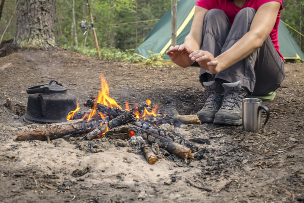 Tyttö istuu telttailun lähellä tulta lämmitetään ja juoda kuumaa teetä
 - Valokuva, kuva
