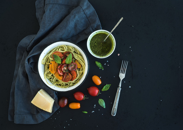 Pasta spaghetti with pesto sauce, basil, slow-roasted cherry-tomatoes in rustic metal bowl on dark grunge backdrop, top view - Photo, Image