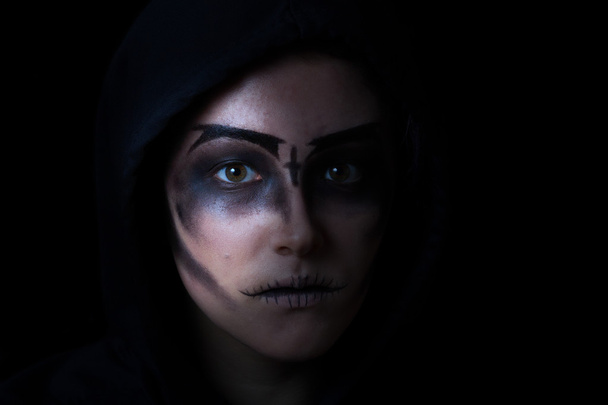 Chica en sudadera con capucha con maquillaje de la cara de miedo sobre fondo negro
 - Foto, Imagen