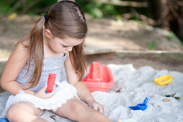 entzückendes kleines Mädchen mit zwei Schwänzen spielt im Sandkasten im schattigen Hinterhof - Foto, Bild