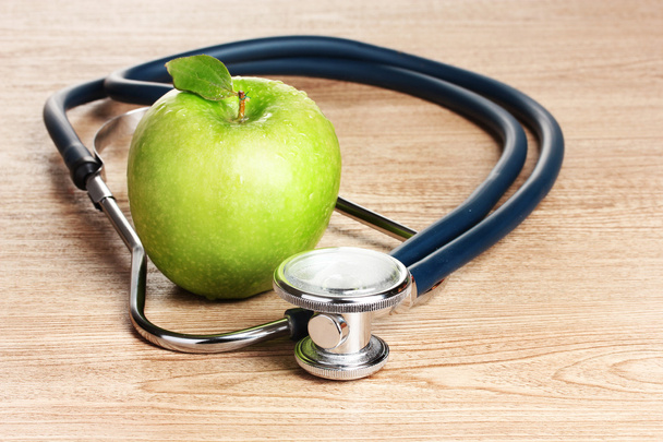 Medical stethoscope and green apple on wooden background - Фото, зображення