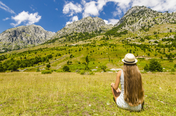 Young woman sitting on a meadow and enjoying the view of mountains - Фото, изображение