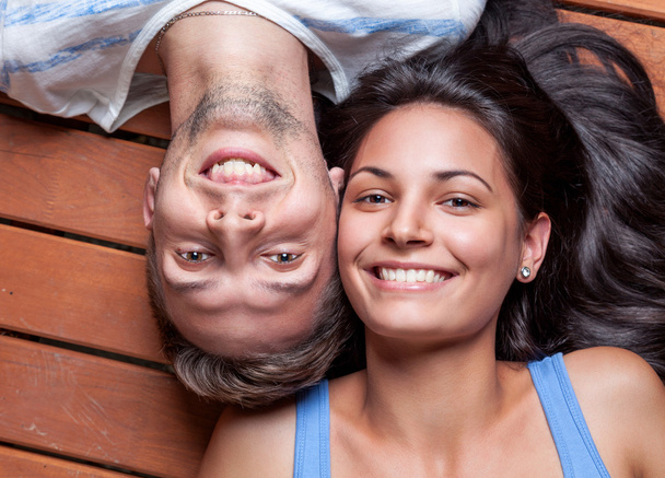 Happy young couple lying on a wooden floor - 写真・画像