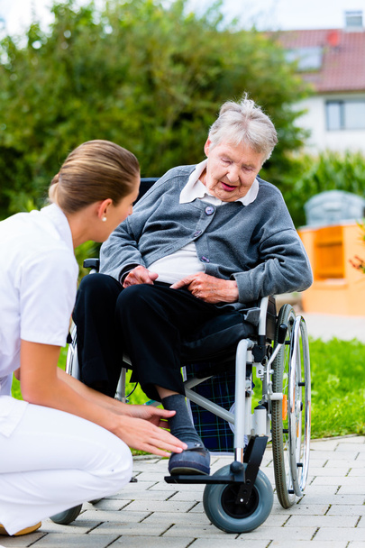 Verpleegkundige duwen senior vrouw in rolstoel op wandeling - Foto, afbeelding