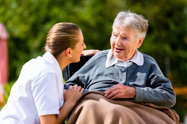Krankenschwester hält Hand an Seniorin im Rollstuhl - Foto, Bild