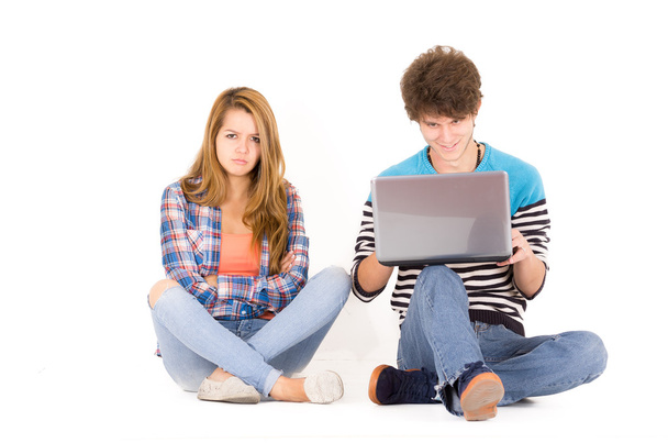 Retrato de atractiva pareja joven en el amor hombre y mujer aislado sobre fondo blanco sentado en el suelo, él mira a la computadora mientras ella está loca
 - Foto, Imagen