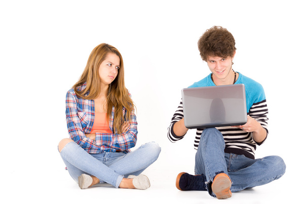 Portrait of attractive young couple in love man and woman isolated over white background sitting on floor, he looks to computer while she is mad - Foto, immagini