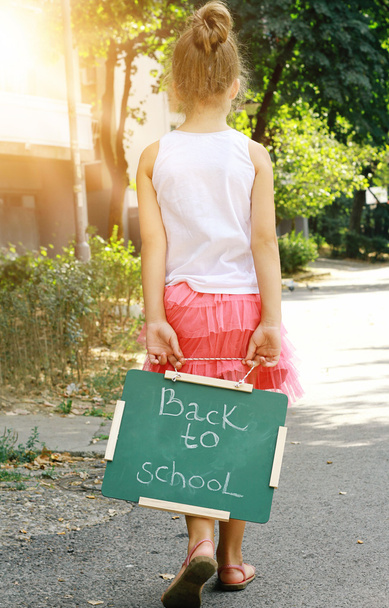 Little girl holding chalkboard with words back to school. Outdoor photo - Foto, imagen