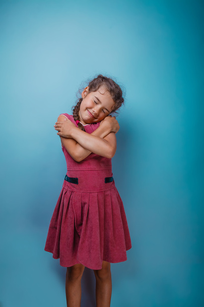 Girl seven years old, European-looking brunette in a pink dress hugging herself shoulders closed her eyes on a gray background, smiling, sleeping - Zdjęcie, obraz