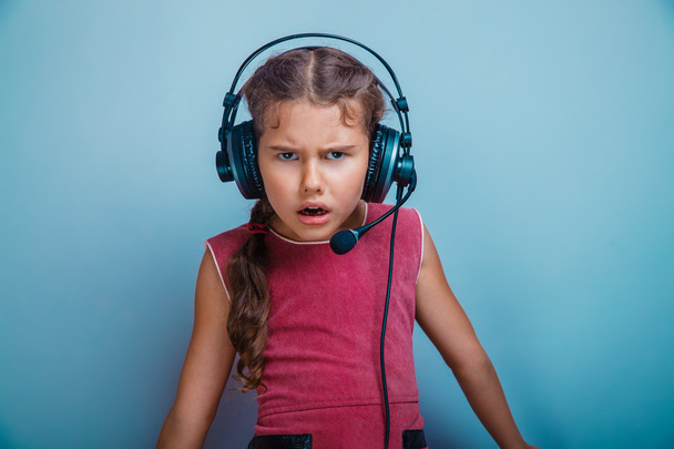 Teen girl child seven years, European appearance brunette in a pink dress in big headphones frowned on a gray background, confusion, anger - Fotoğraf, Görsel