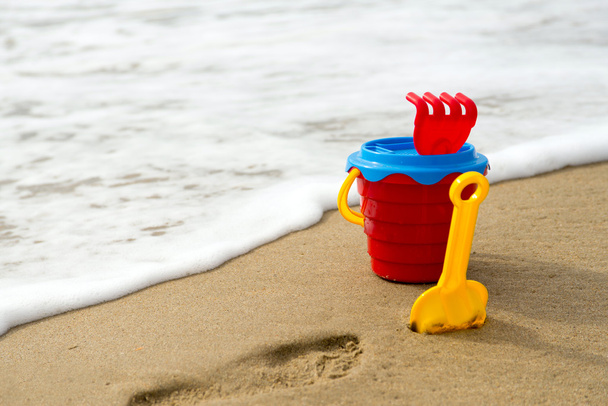 Красное ведро с лопатой, грабли и сеткой на пляже
 - Фото, изображение