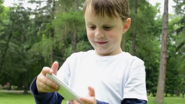 young little boy plays games on smartphone - park - Filmati, video