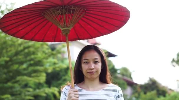 Asian girl with red oriental style umbrella on green nature background - Filmati, video