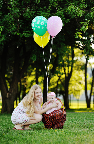 Daughter with her mother relaxing in the park on the grass. little girl in the basket with balloons - Foto, afbeelding
