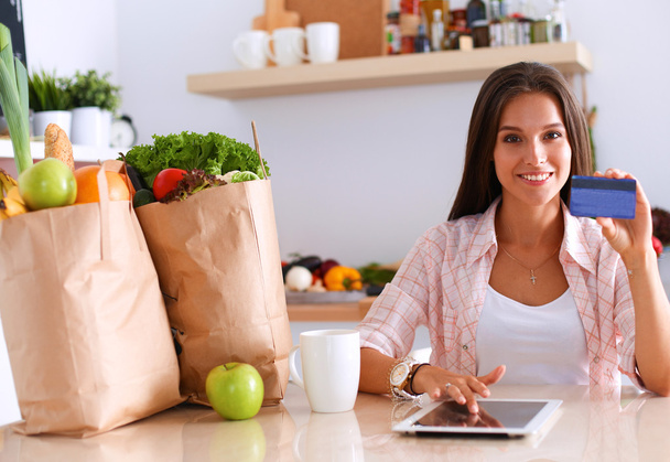 Smiling woman online shopping using tablet and credit card in kitchen - Foto, Bild
