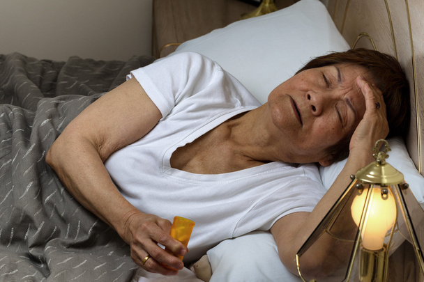 Senior woman preparing to take medicine at nighttime due to inso - Photo, Image