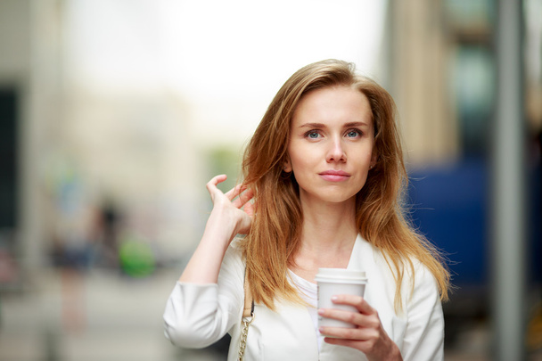 Young woman with coffe-to-go in street. Defocused background. - Фото, изображение