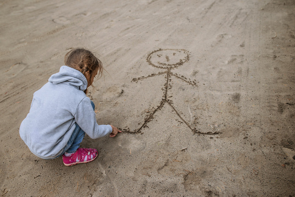 Маленька дівчинка пісок малює смішного чоловіка
 - Фото, зображення