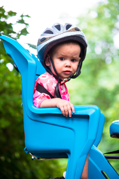 Bambina vestita con casco da bicicletta e si siede su un seggiolino per bicicletta
 - Foto, immagini