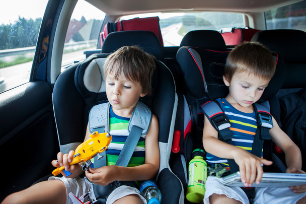 Two boy in car seats, traveling in car and playing with toys and - Φωτογραφία, εικόνα