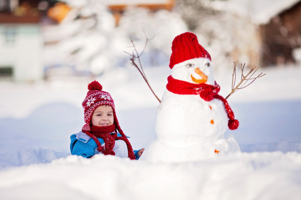 Happy beautiful child building snowman in garden, winter - Valokuva, kuva