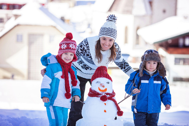 Happy beautiful family building snowman in garden, winter time,  - Zdjęcie, obraz