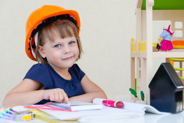 Lächelndes kleines Mädchen mit orangefarbenem Schutzhelm - spielender Ingenieur oder Bauarbeiter - Foto, Bild