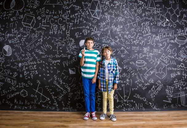 Cute little boy and girl in front of a big blackboard. - Fotografie, Obrázek