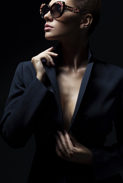 Porträt eines schönen Mädchens, das in schwarzer Jacke und modischer Sonnenbrille im Studio posiert. das Konzept der stilvollen und sexy Frauen. perfekte Haut und Körper - Foto, Bild