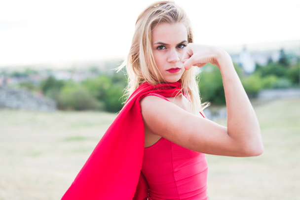 Vertrouwen blonde vrouw in rood kostuum weergegeven: spier- en kracht - Foto, afbeelding