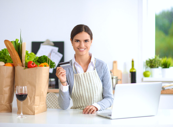 Smiling woman online shopping using computer and credit card in kitchen - Фото, зображення