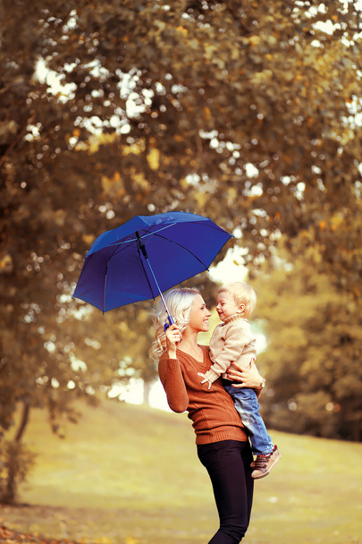 Family in autumn! Happy mother and child with umbrella having fu - Фото, зображення