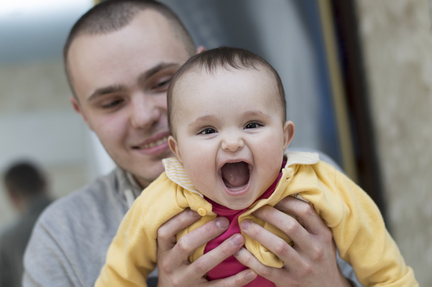 Молодий батько чоловік тримає і обіймає в руках дитину дитина дівчинка смердить сміючись
 - Фото, зображення