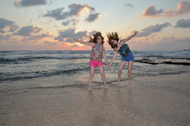 Дві блондинки стрибають на пляжі на заході сонця
 - Фото, зображення