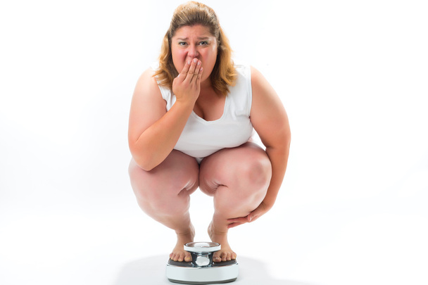 Obese young woman crouching on a scale - Photo, Image