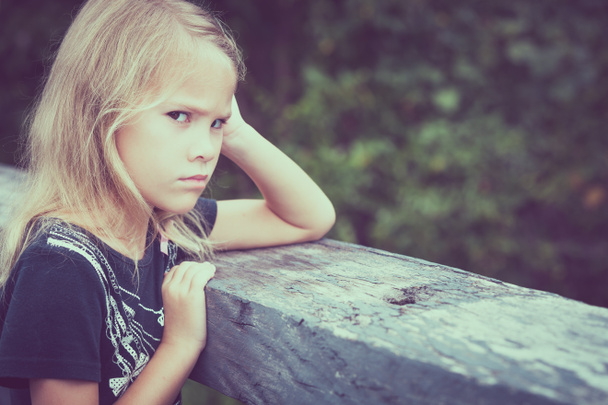 Portrait of sad blond little girl sitting on the bridge - Zdjęcie, obraz